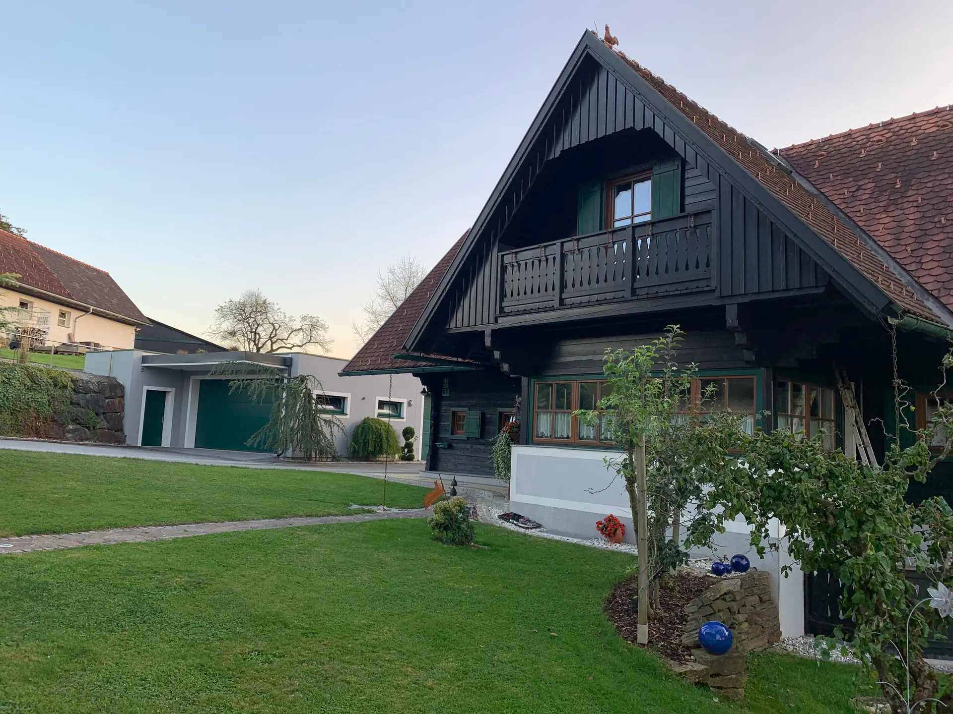 Blockhaus mit Balkon im Abendlicht, davor Rasen und Gartenweg