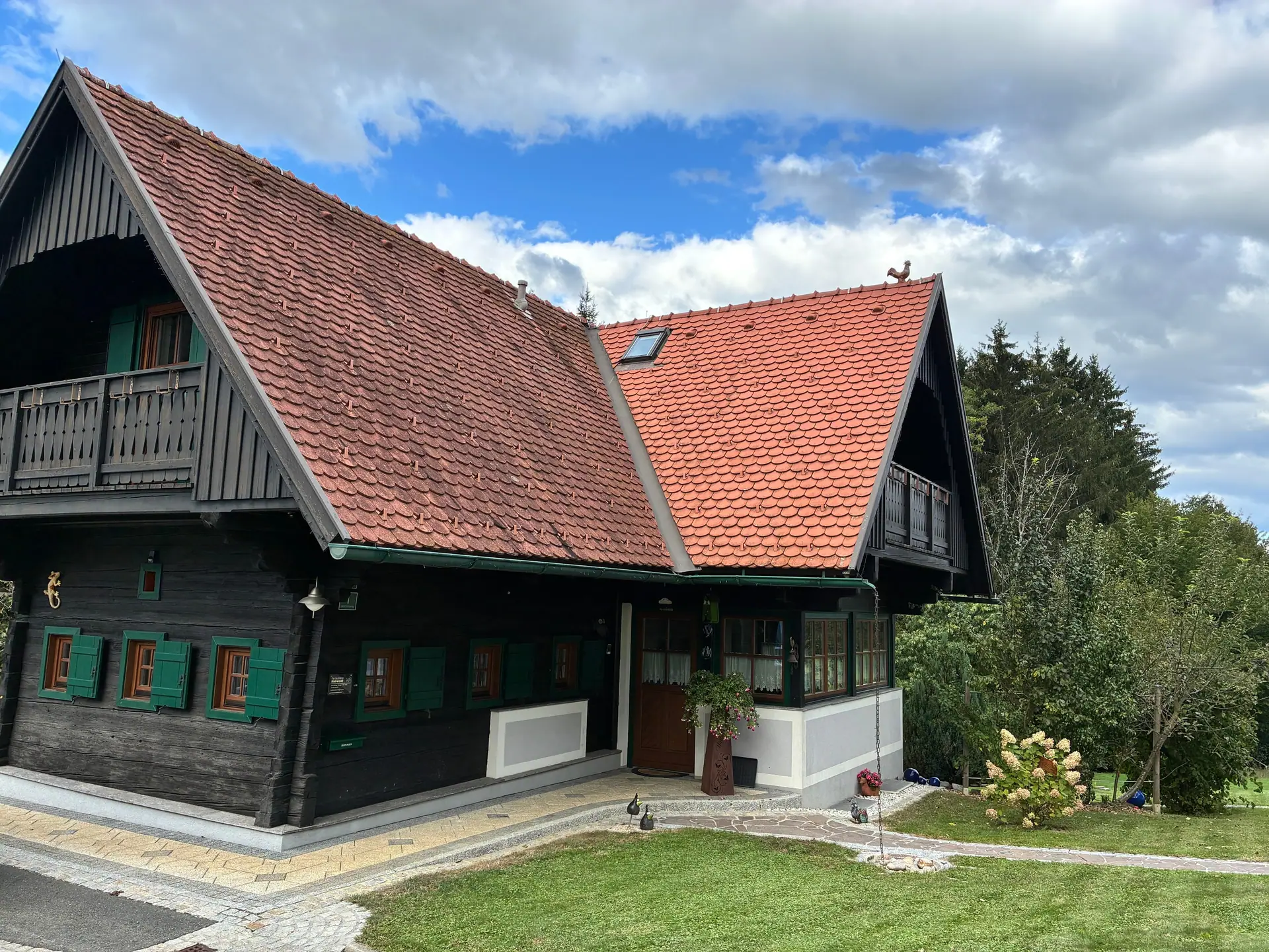 Blockhaus aus dunklem Holz mit rotem Ziegeldach, grünen Fensterläden und Holzbalkon