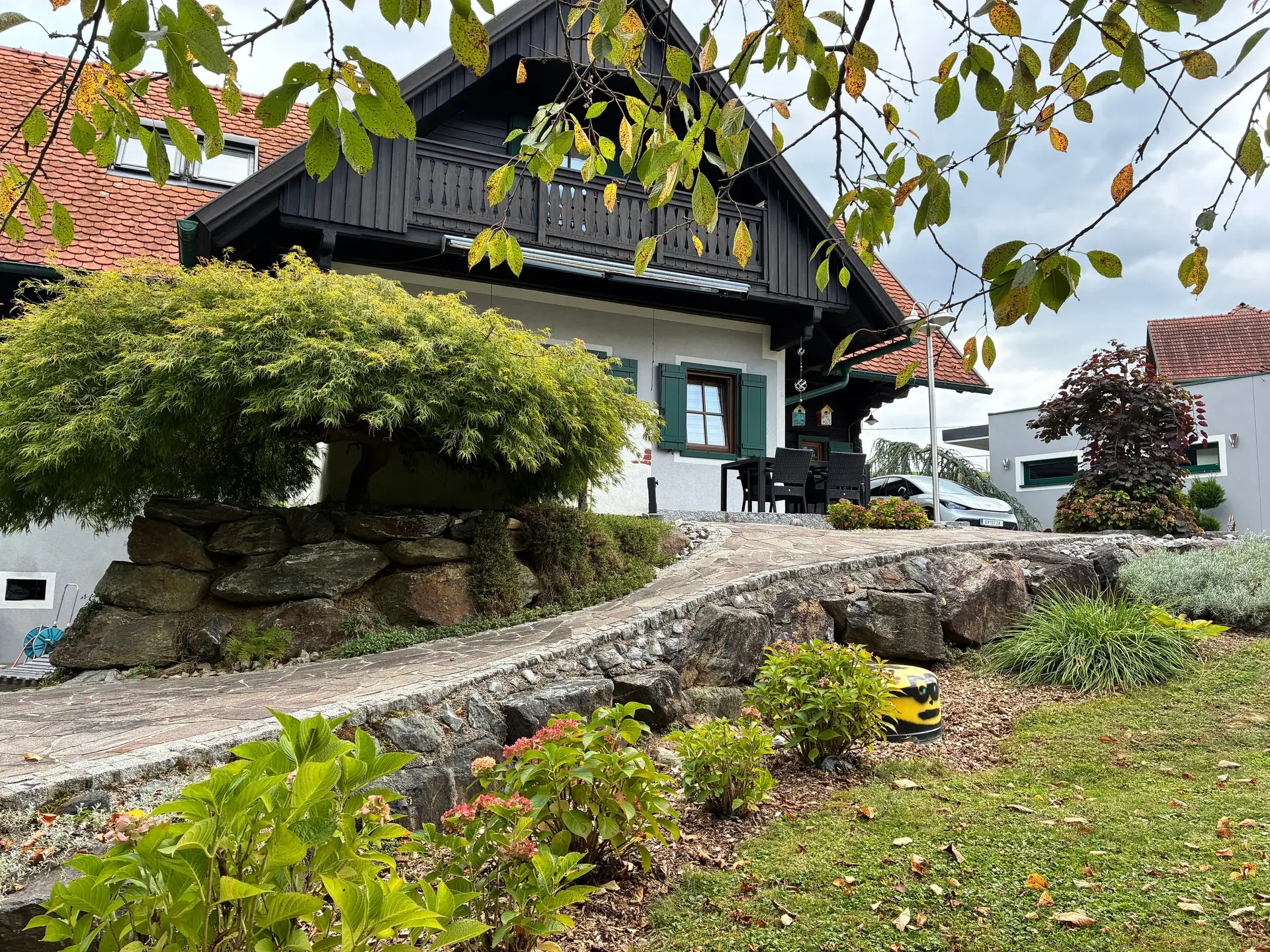 Natursteinmauer und gepflasterter Weg, dahinter das Haus mit Balkon