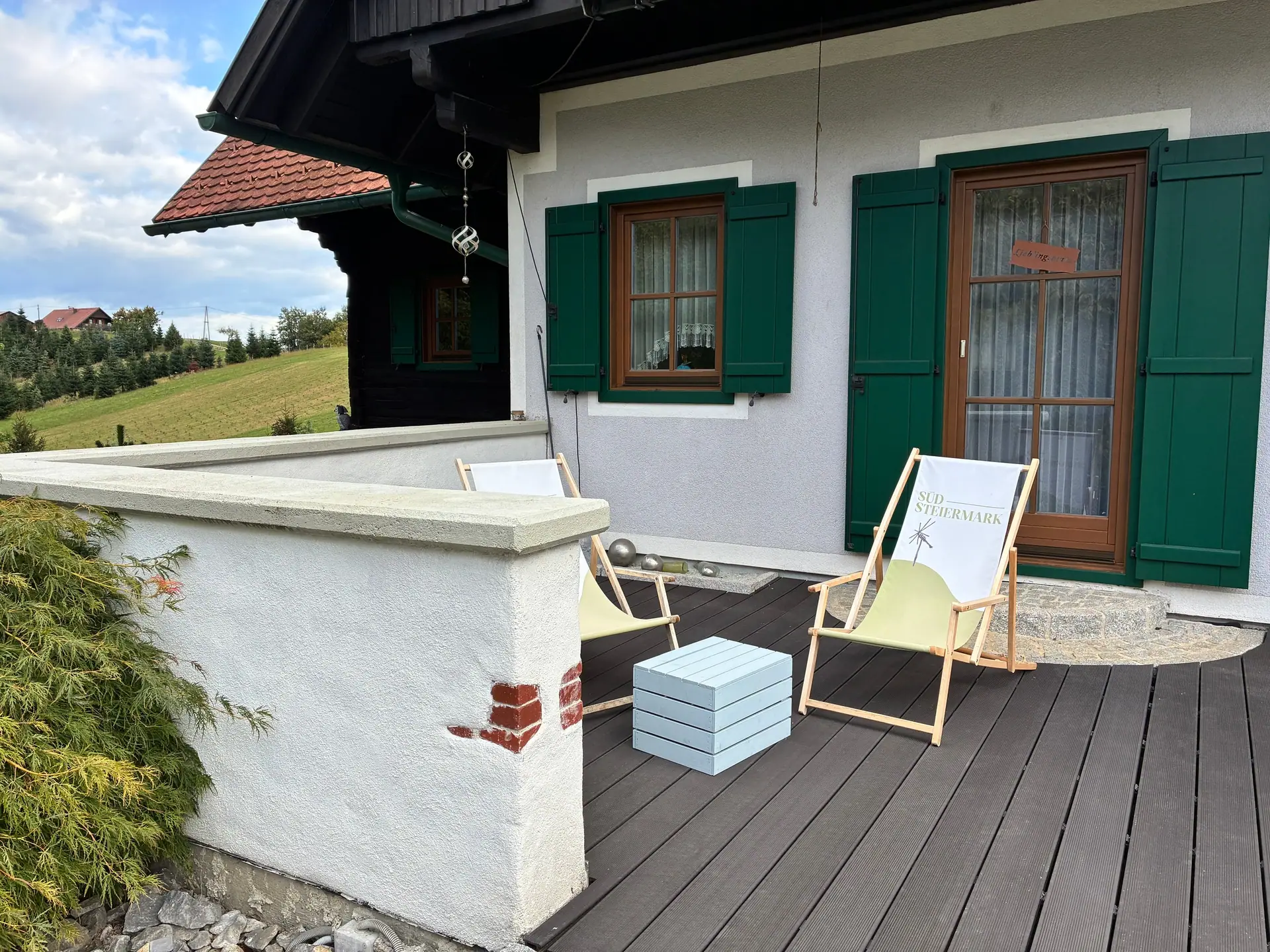 Terrasse mit Holzboden und zwei Liegestühlen vor weiß verputzter Wand mit grünen Fensterläden