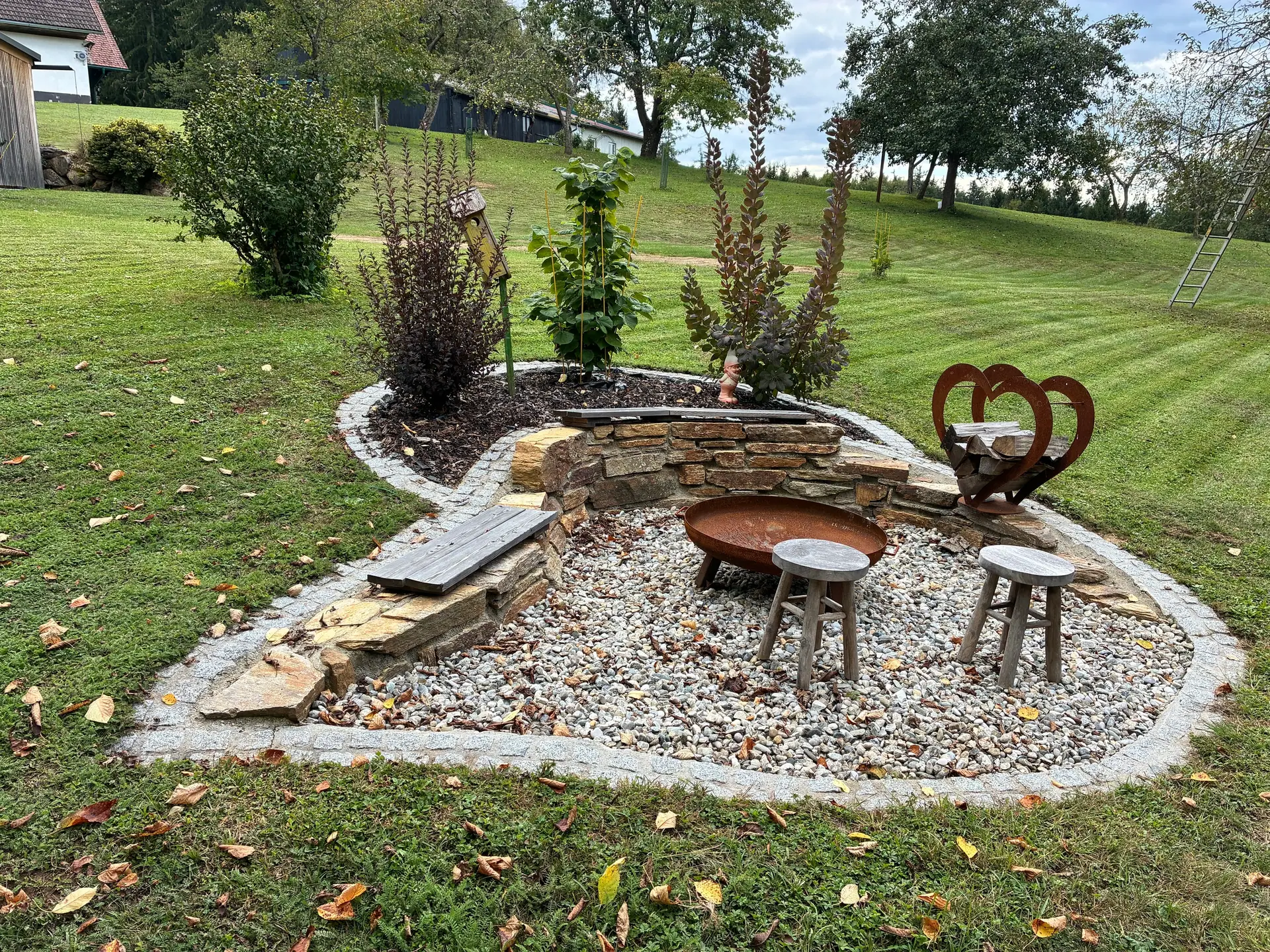 Feuerstelle mit Sitzhockern in einem Kiesbett auf der Wiese